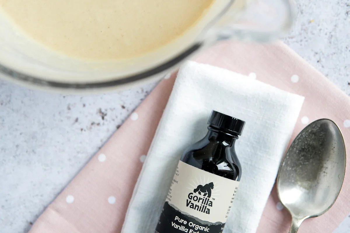 Organic vanilla extract bottle with tarnished spoon on polka-dot napkin beside mixing bowl — gourmand note still life
