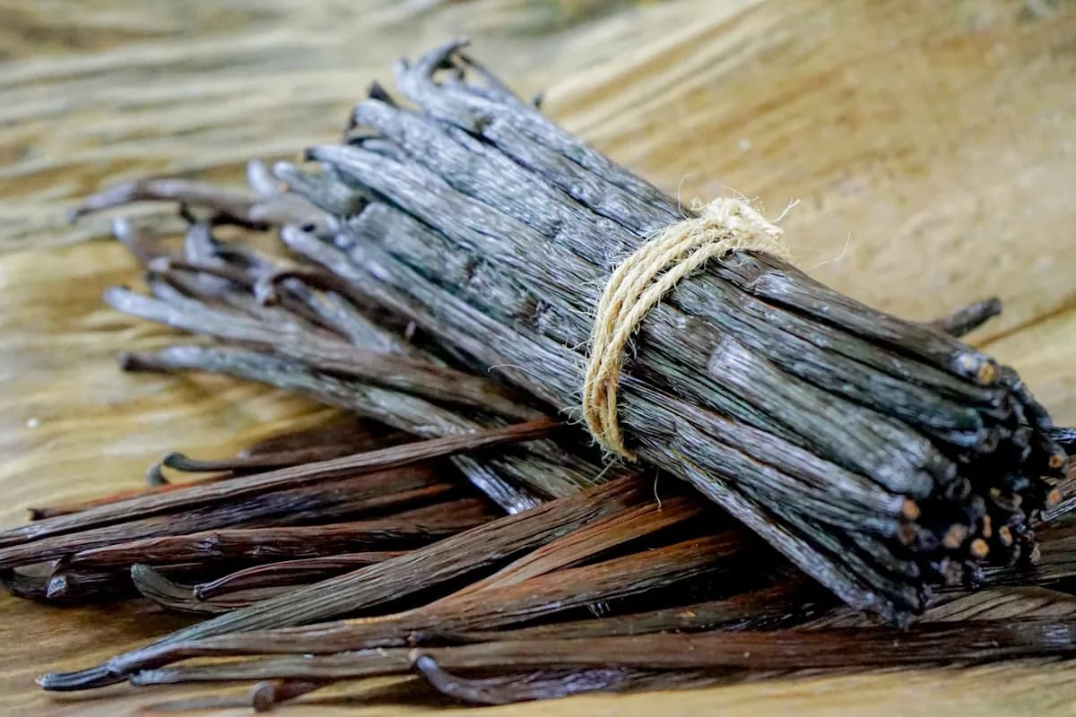 Dried Madagascar vanilla pods on a light wooden board — budget gourmand note still life