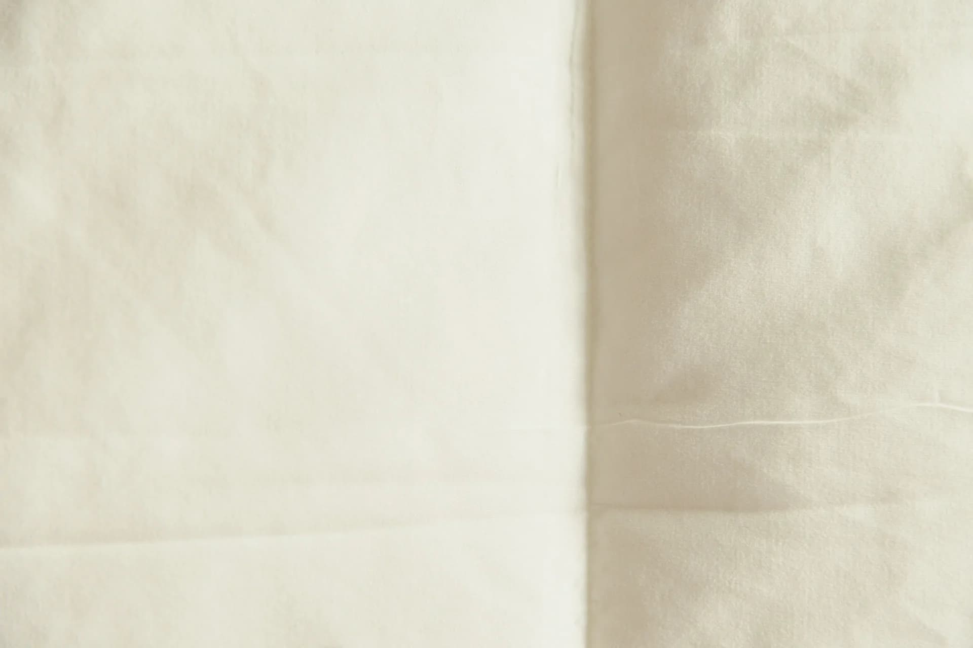 Cream-colored linen fabric with soft folds in warm window light — intimate skin-scent mood
